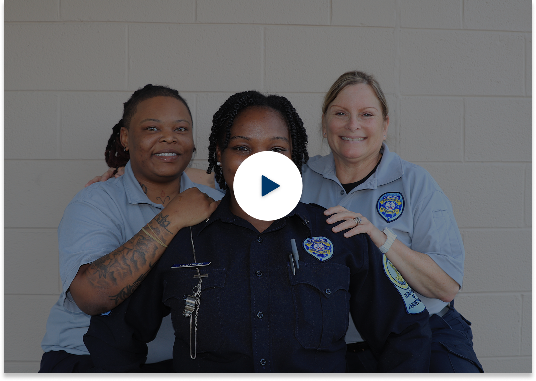 Tres agentes penitenciarias de pie contra la pared y el icono de juego en el centro de la imagen.